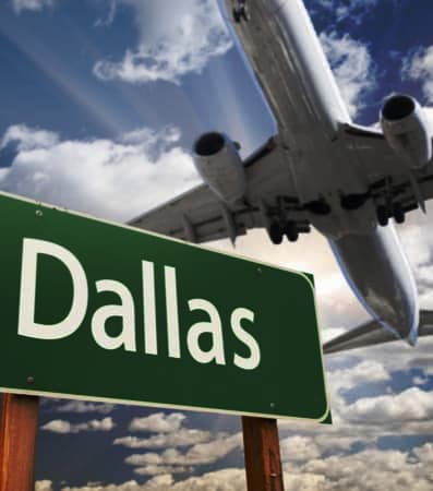 A plane flying over a green street sign reading "Dallas"